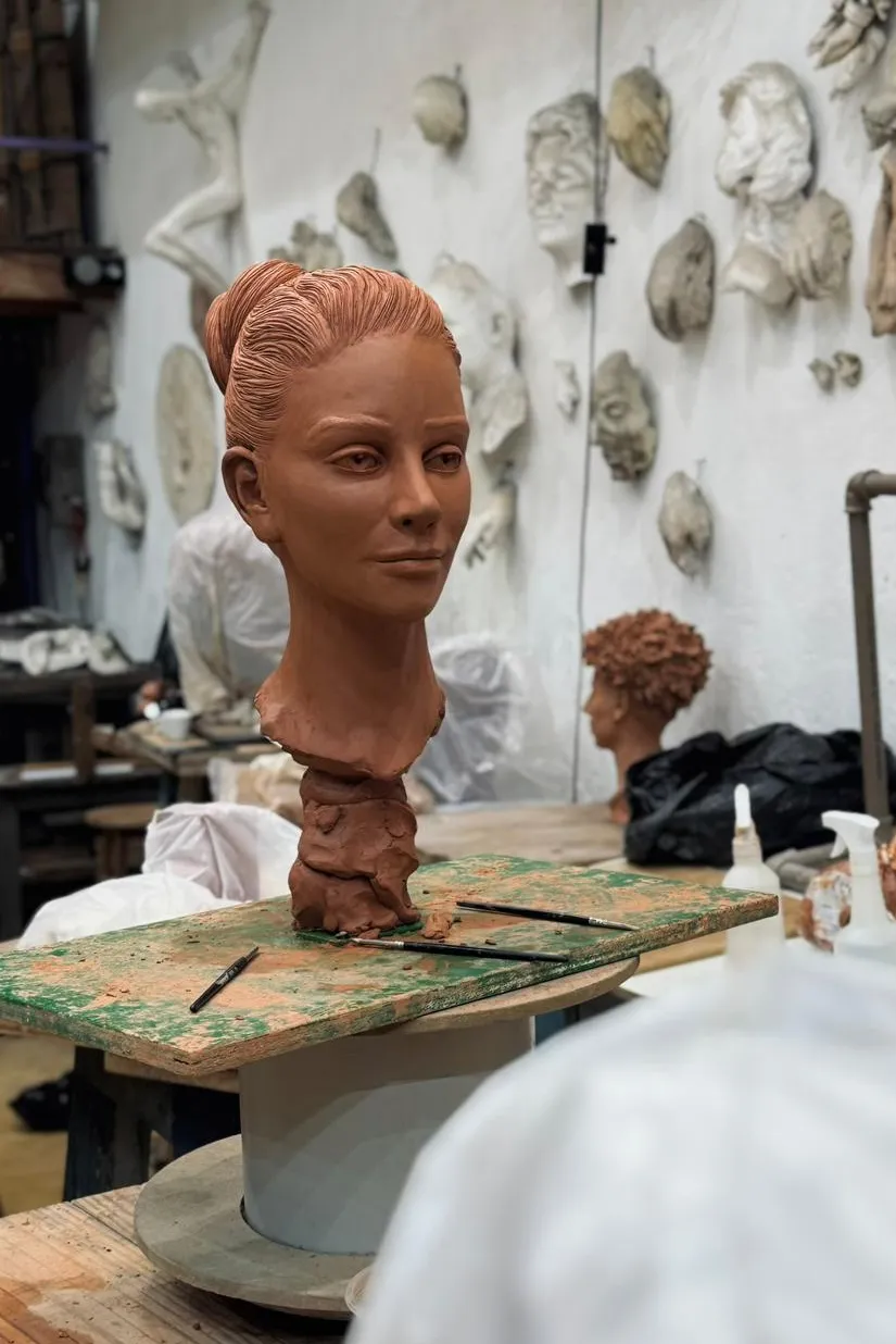 Busto em cerâmica no ateliê, com peças na parede ao fundo